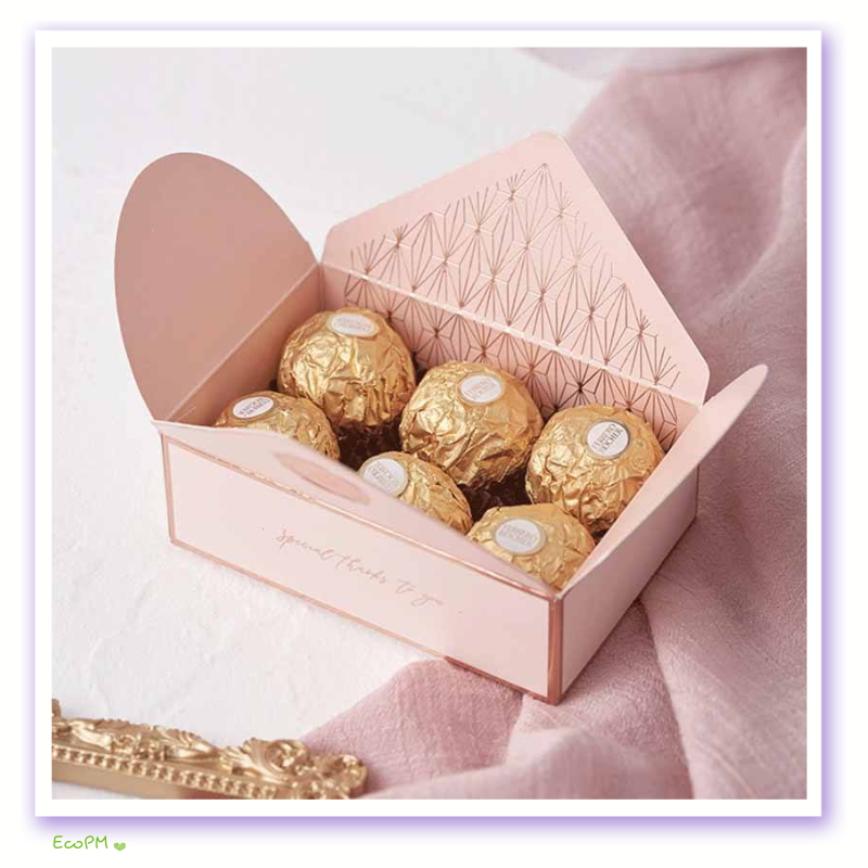 blush-treasure-favor-box-golden-sweets.png Open blush pink favor box filled with golden wrapped candies, intricate geometric patterns inside, epitomizing refined taste.