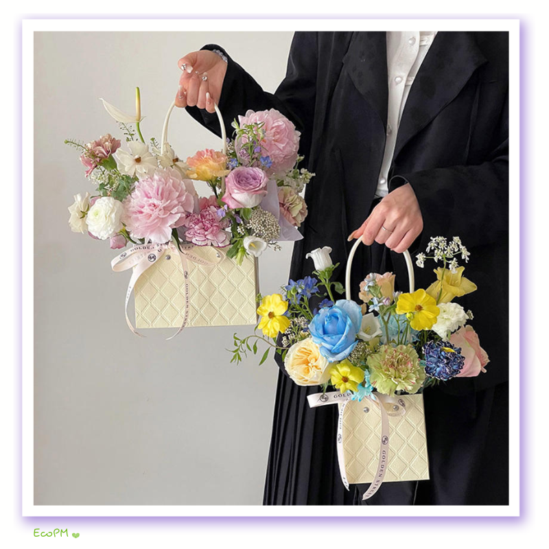 eco-chic-floral-gift-bags.jpg A person in a black coat holding two eco-chic paper gift bags with a quilted pattern, filled with an assortment of pink, yellow, and blue flowers.