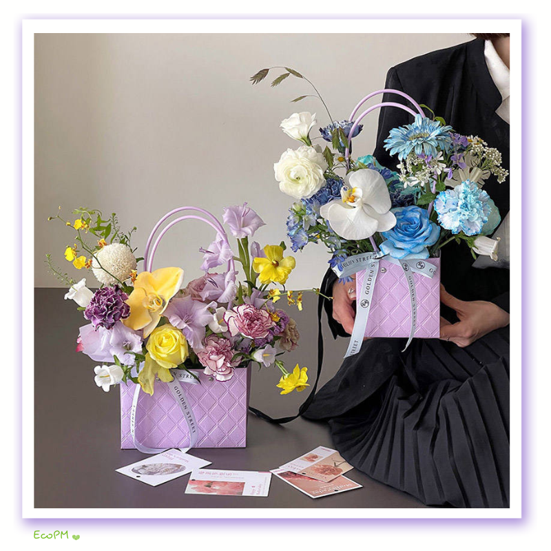 vibrant-flower-arrangement-paper-bag.jpg Vibrant floral arrangement in a purple paper bag held by an individual in a black dress, showcasing a mix of yellow, blue, and purple flowers.