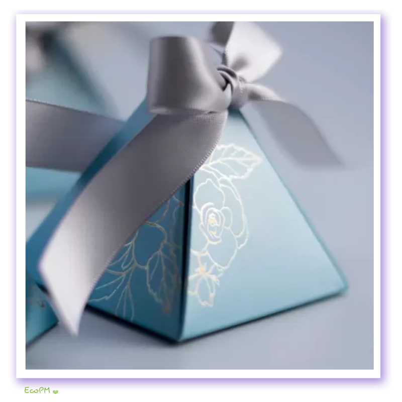 close-up-elegant-pyramid-favor-box-satin-ribbon.png Close-up view of an elegant blue pyramid favor box with a gold floral design and a gray satin ribbon, ideal for sophisticated gifting.