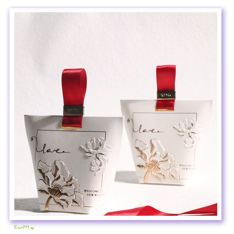embossed-floral-wedding-favor-boxes.png Elegant wedding favor boxes with embossed floral design and red ribbon handles, inscribed with