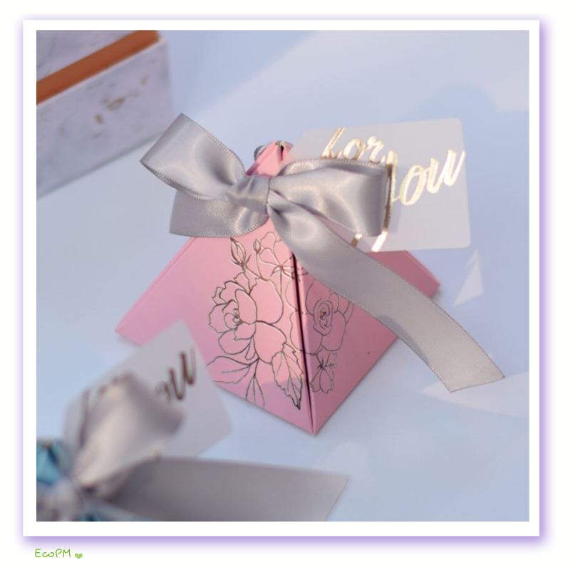 pink-floral-pyramid-favor-box-satin-ribbon.png A delicate pink pyramid favor box adorned with a silver satin ribbon and an intricate floral design, accompanied by a stylish 'for you' card, perfect for weddings and special events.