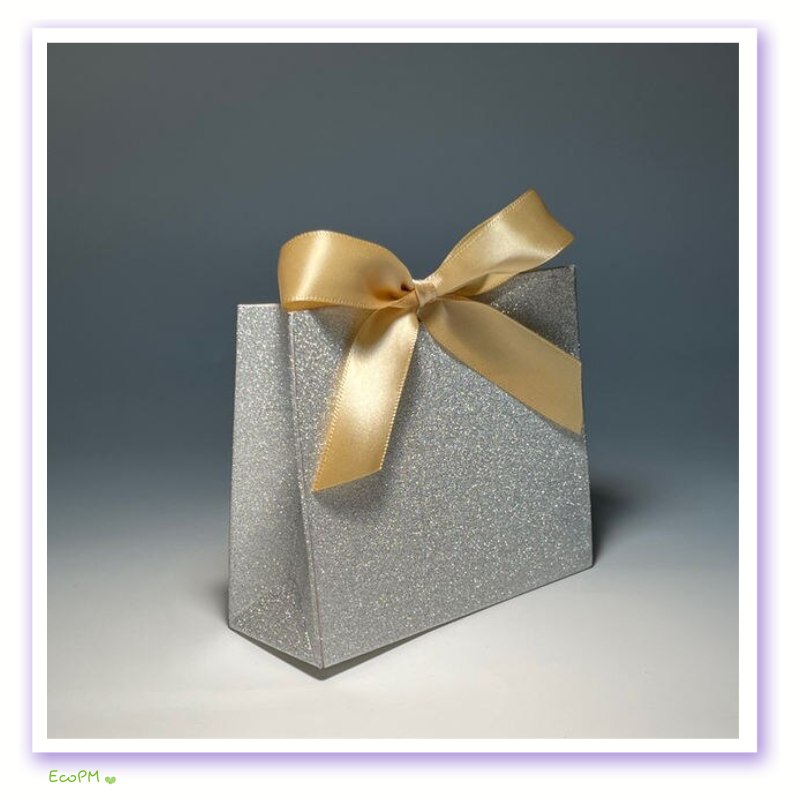 silver-glitter-favor-box-with-gold-ribbon.png A silver glitter favor box adorned with a golden satin ribbon bow, set against a soft background.