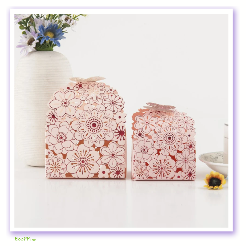 elegant-pink-floral-cut-out-favor-boxes.png Two pink floral cut-out favor boxes with butterfly closures, displayed next to a white vase with blue flowers.
