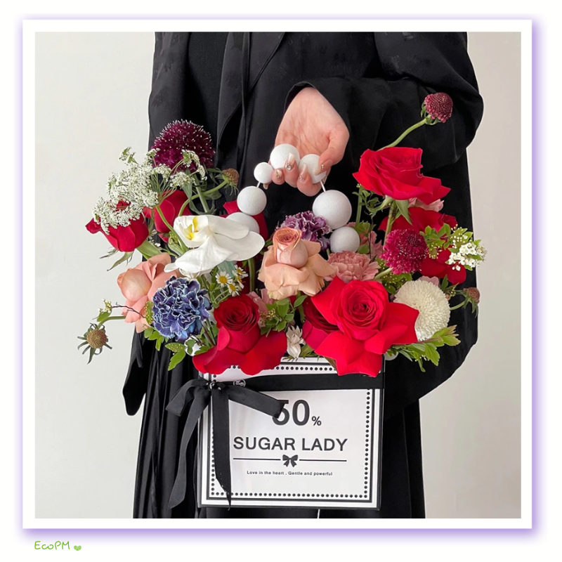 sugar-lady-floral-box.png A person in black attire holding a sophisticated flower box with the inscription