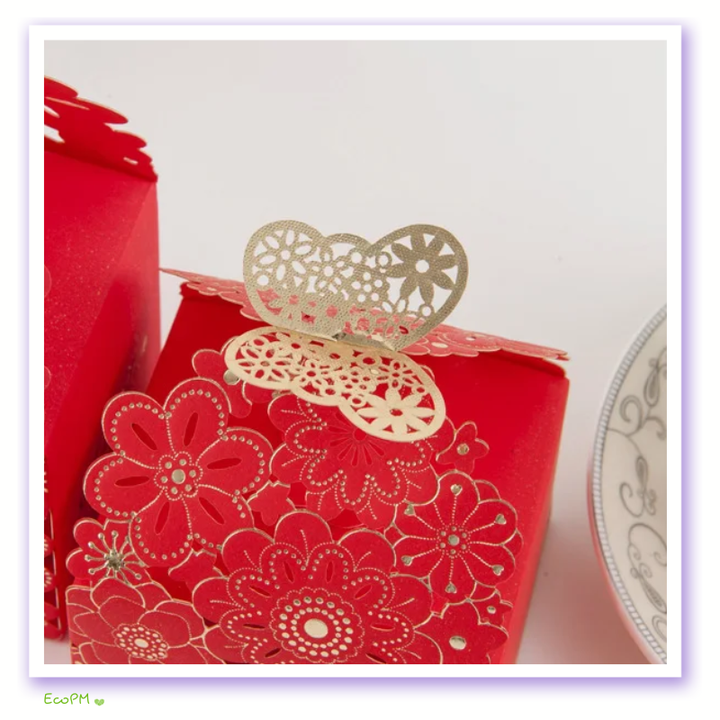vibrant-red-floral-laser-cut-favor-boxes.png Vibrant red favor boxes with delicate floral laser-cut design and elegant gold heart clasps on a soft background.