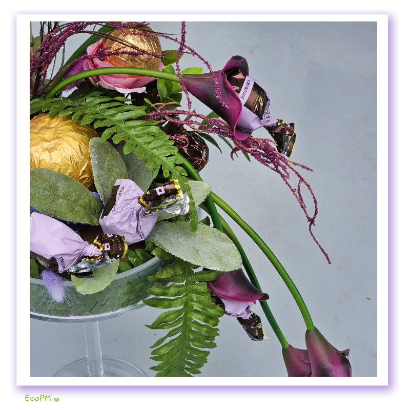 elegant-enchantment-chocolate-arrangement-side-view.jpg Side view of the Elegant Enchantment Chocolate Arrangement, displaying premium chocolates and lush greenery in an elegant glass vase.
